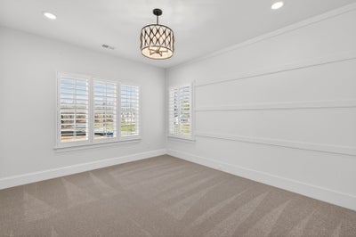 Empty room with white shiplap walls, beige carpet, plantation shutters, and decorative pendant light