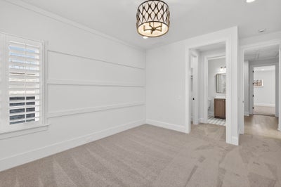 Empty bedroom with white shiplap accent wall, beige carpet, and decorative ceiling light fixture