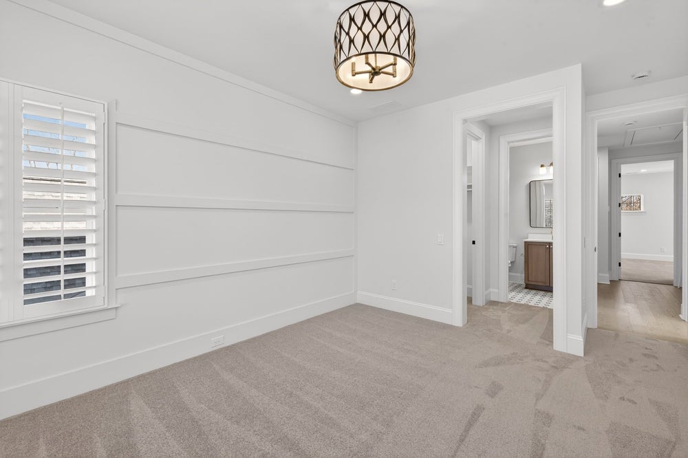 Empty bedroom with white shiplap accent wall, beige carpet, and decorative ceiling light fixture