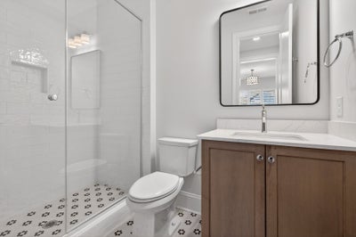 Modern bathroom with wood vanity, white countertop, glass shower, and patterned tile floor