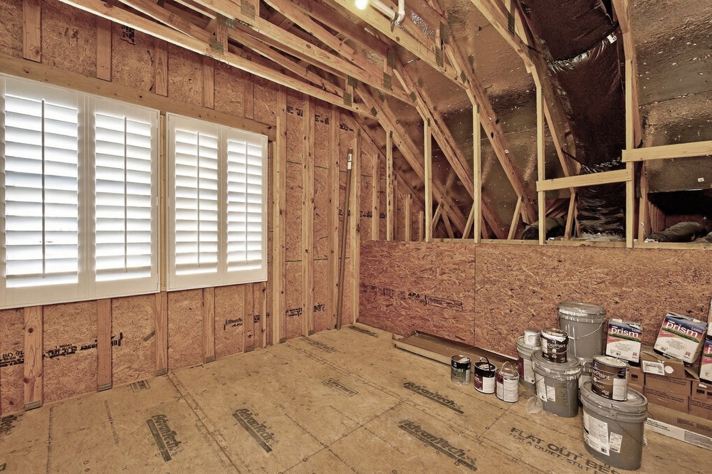 Unfinished room under construction with exposed wood framing, shuttered windows, and paint supplies on floor