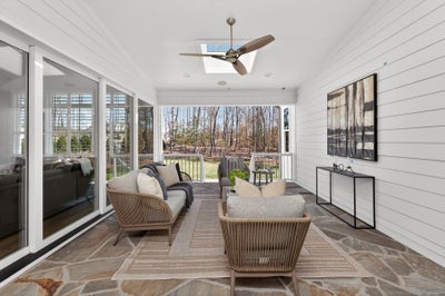 Screened porch with stone flooring, ceiling fan, and outdoor furniture overlooking wooded backyard