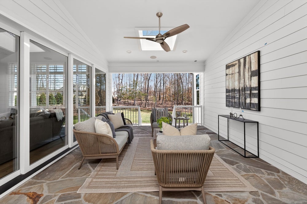 Screened porch with stone flooring, ceiling fan, and outdoor furniture overlooking wooded backyard