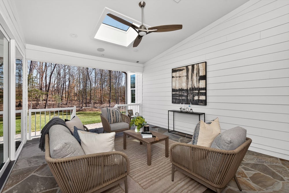 Screened porch with shiplap walls, ceiling fan, skylight, and outdoor furniture overlooking wooded backyard