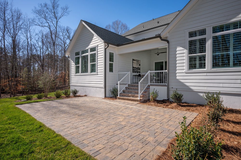 White siding home with covered porch, brick paver patio, and landscaped yard