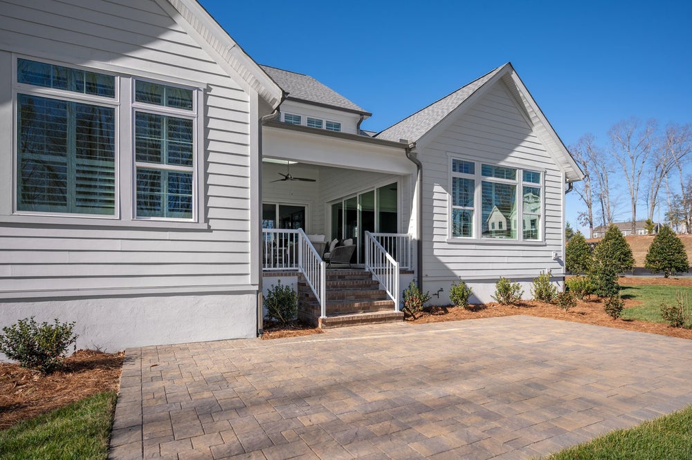White siding home with covered porch, brick stairs, and paver patio