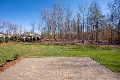 Brick paver patio overlooking large grassy backyard with wooded area