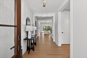 Bright entryway hallway with hardwood floors and white walls leading to open living space