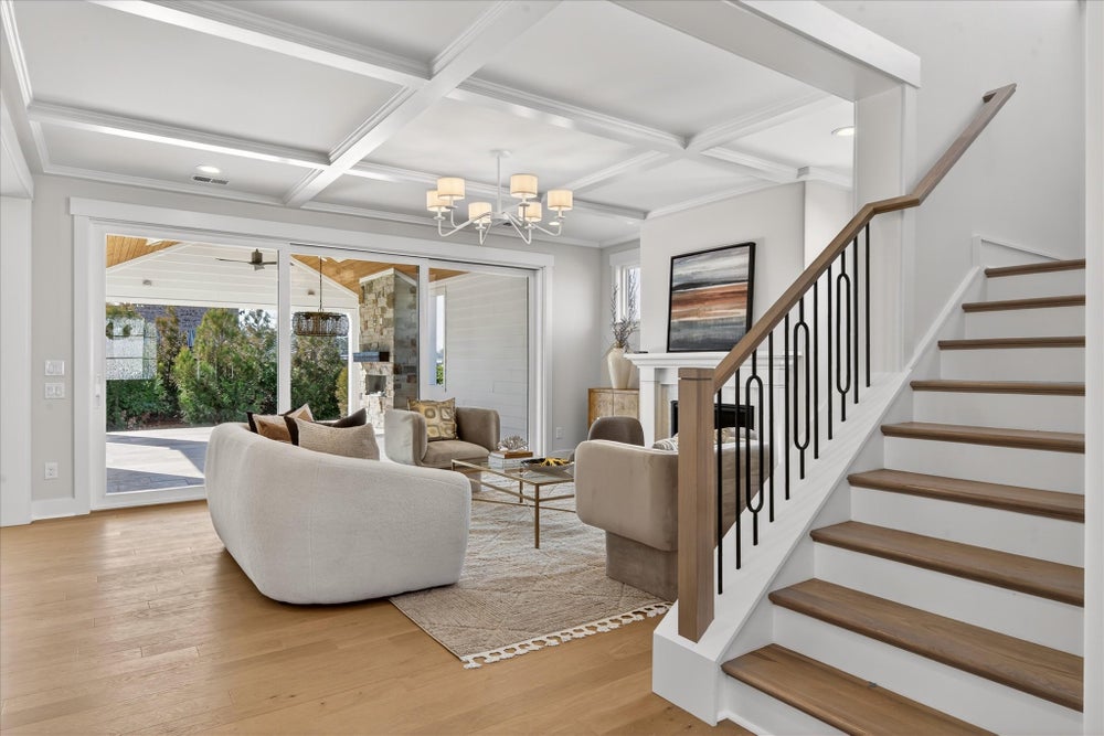 Living room with coffered ceiling, hardwood floors, and staircase leading to patio doors