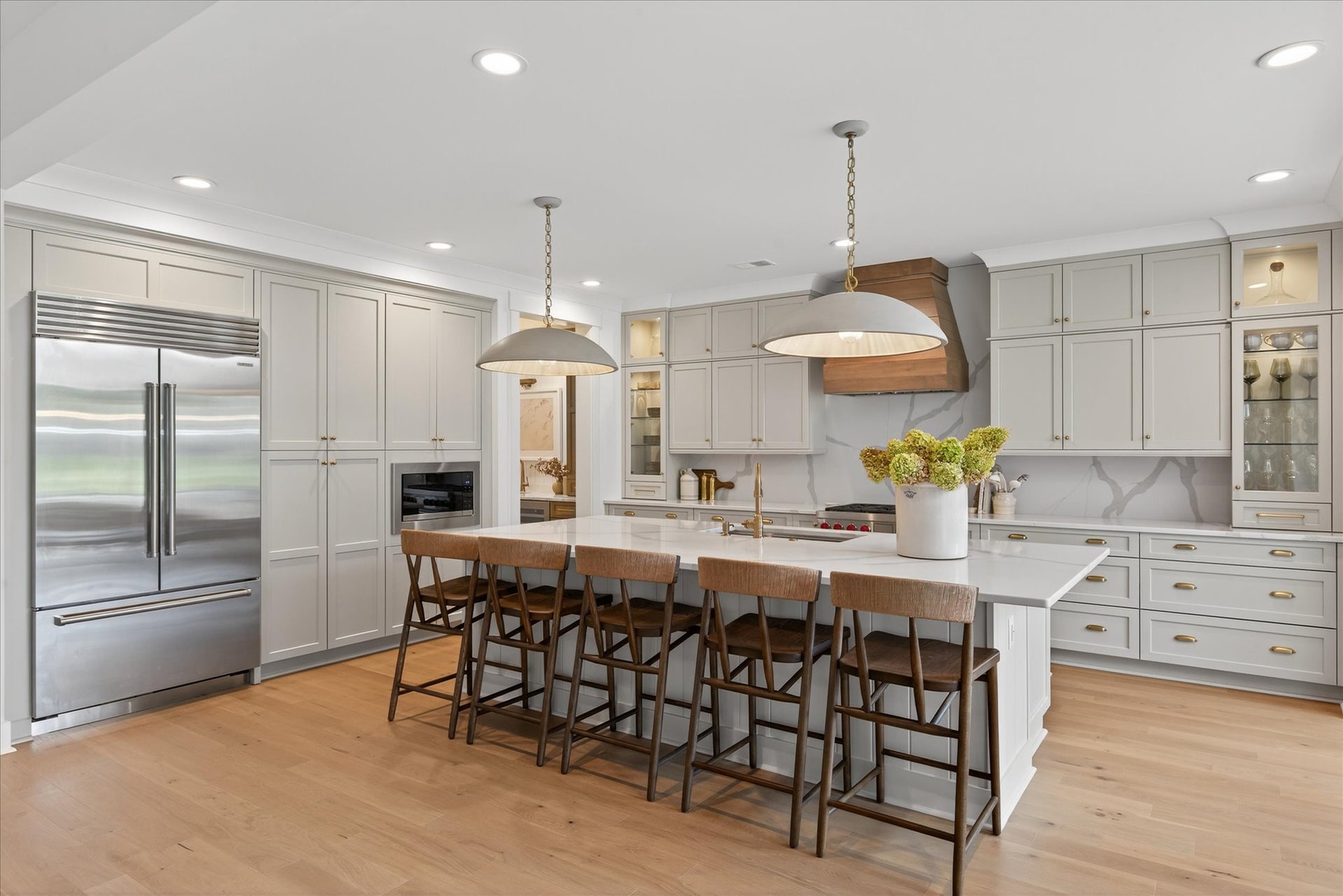 Large kitchen with white cabinets, center island with seating, wood range hood, and stainless steel appliances