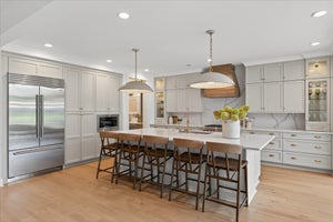Large kitchen with white cabinets, center island with seating, wood range hood, and stainless steel appliances