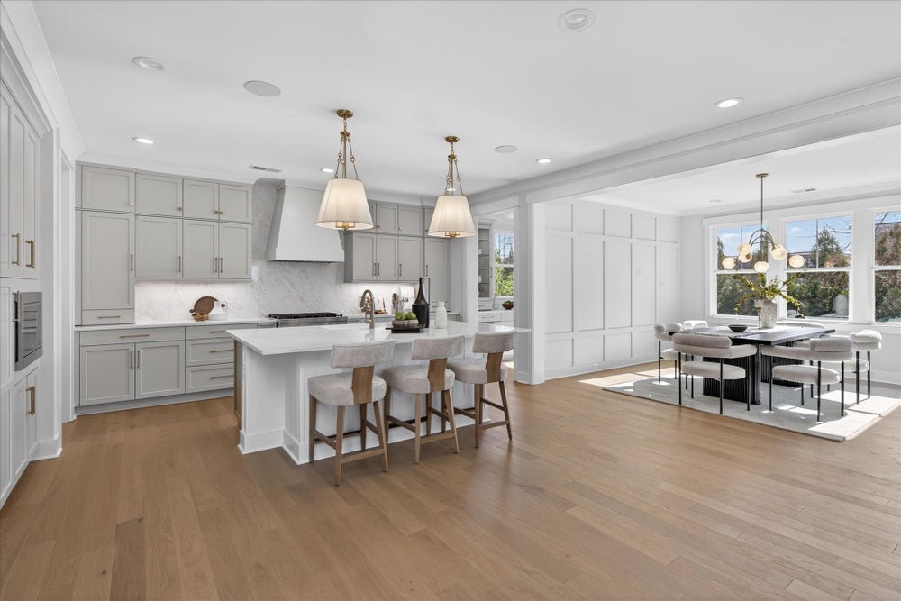 Open-concept kitchen and dining area with white cabinets, marble countertops, and light hardwood floors