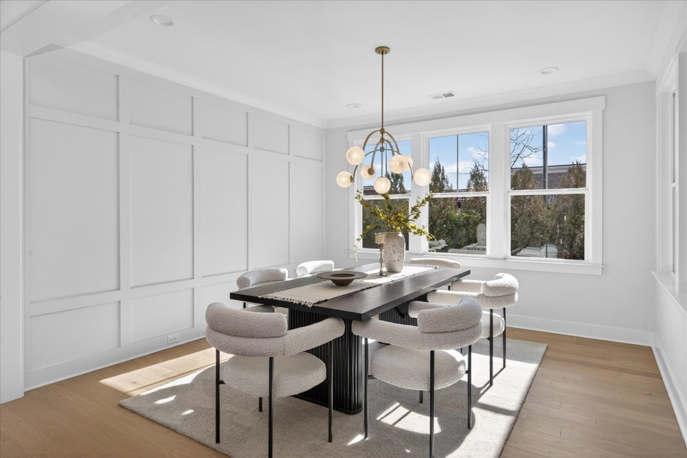 Dining room with white wainscoting, modern chandelier, and large windows overlooking trees