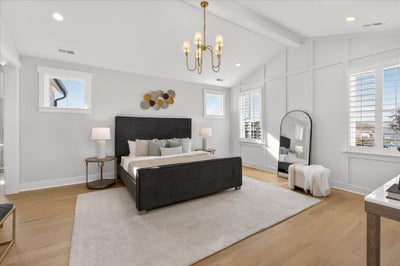 Spacious master bedroom with black bed frame, white walls, hardwood floors, and brass chandelier