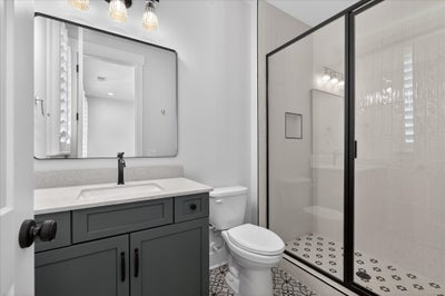 Modern bathroom with gray vanity, black-framed mirror, and glass-enclosed shower with patterned tile floor