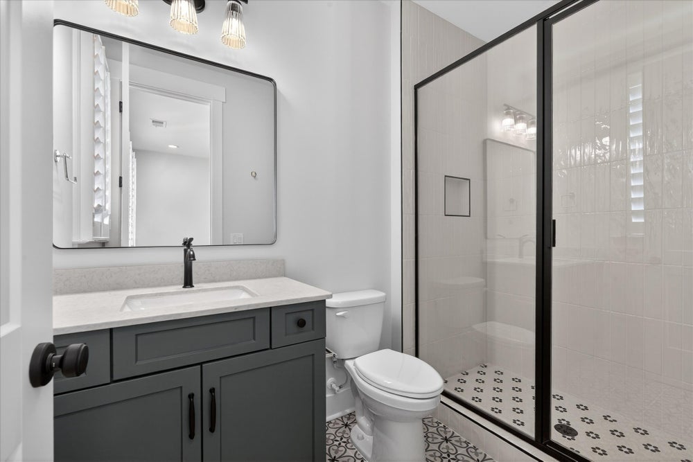 Modern bathroom with gray vanity, black-framed mirror, and glass-enclosed shower with patterned tile floor
