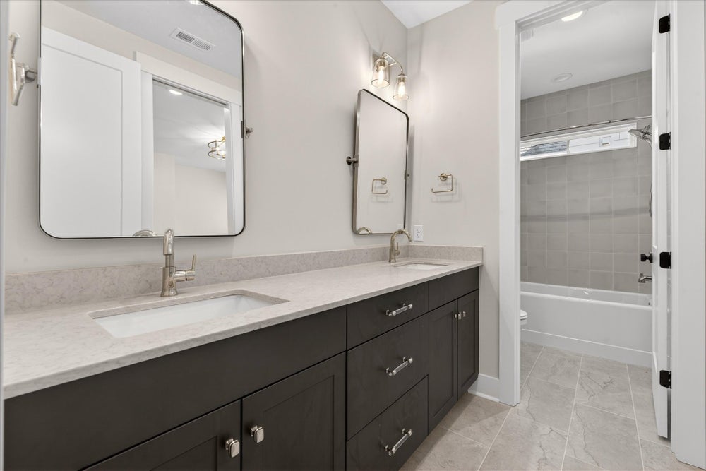 Bathroom with double vanity, dark gray cabinets, white countertops, and tub-shower combo