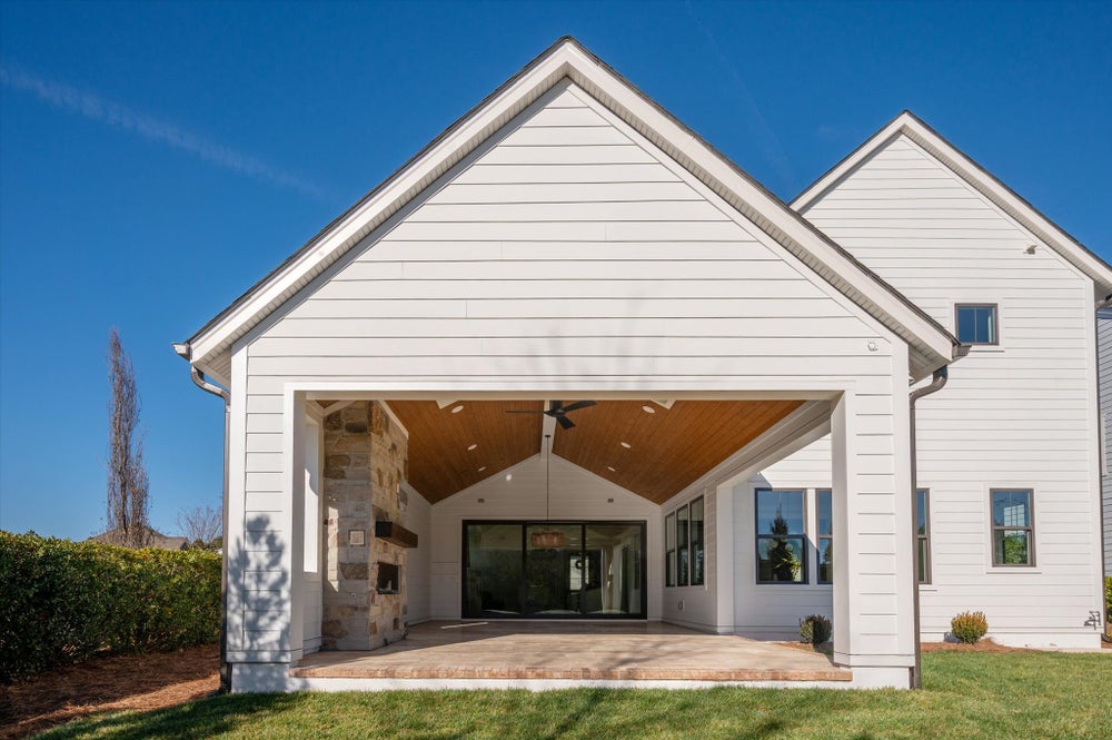 White farmhouse with covered porch featuring wood ceiling and stone fireplace