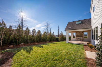 Backyard with covered patio, fireplace, and landscaped lawn with tree border
