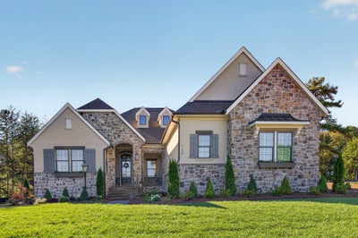 Two-story home with stone and stucco exterior, arched entry, gray shutters, and manicured front lawn