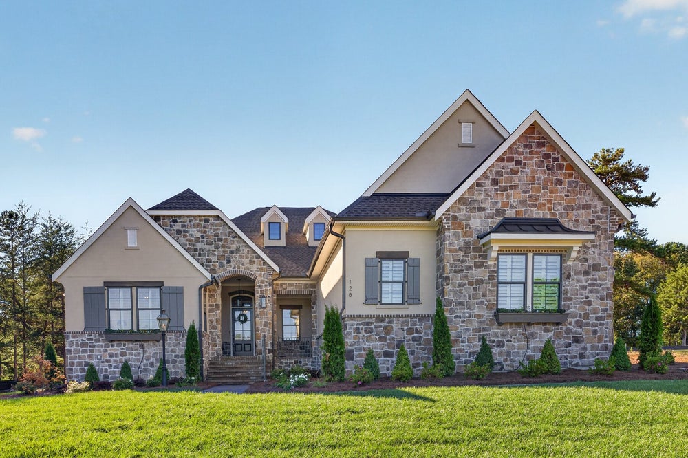 Two-story home with stone and stucco exterior, arched entry, gray shutters, and manicured front lawn