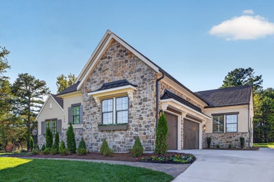 Stone and stucco home with two-car garage, peaked roofline, and landscaped front yard