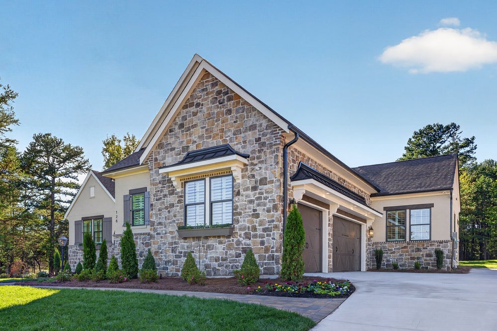 Stone and stucco home with two-car garage, peaked roofline, and landscaped front yard