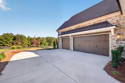 Three-car garage with brown carriage-style doors on a stone exterior home with wide concrete driveway