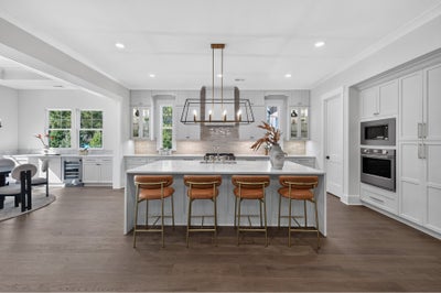 Large kitchen with gray cabinets, white island, four leather barstools, and a bronze pendant light over hardwood floors