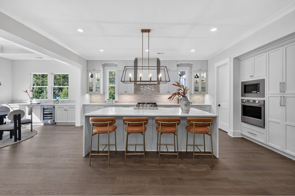 Large kitchen with gray cabinets, white island, four leather barstools, and a bronze pendant light over hardwood floors