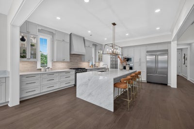 Large kitchen with gray cabinets, marble island with bar stools, and dark hardwood floors