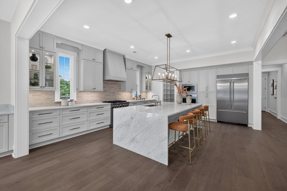 Large kitchen with gray cabinets, marble island with bar stools, and dark hardwood floors