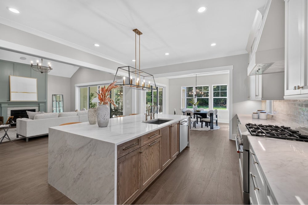 Open-concept kitchen with large marble island, white cabinets, and hardwood floors opening to living and dining areas