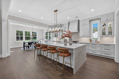 Open kitchen with large marble island, four bar stools, gray cabinets, and hardwood floors open to dining area