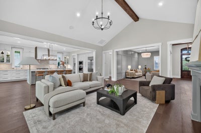 Open-concept living room with vaulted ceiling, wood beam, and view into white kitchen with island