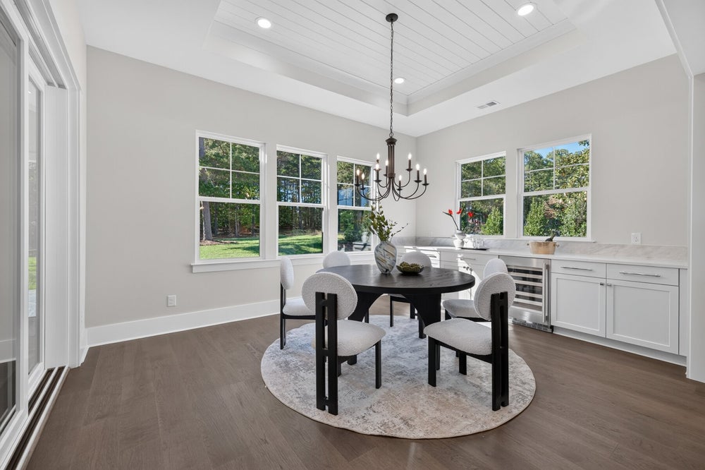 Dining room with round dark wood table, chandelier, hardwood floors, and built-in wet bar with white cabinets