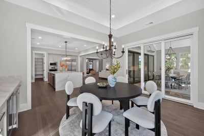 Open-concept dining area with round dark table, white chairs, chandelier, and sliding glass doors to patio