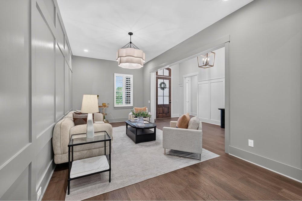 Formal sitting room with gray wainscoting, hardwood floors, and pendant light, open to entry foyer with wood front door.