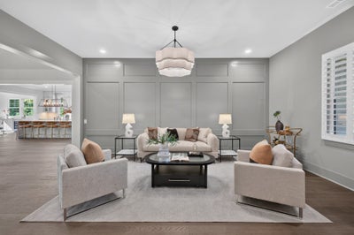 Living room with gray panel walls, neutral seating, dark coffee table, and pendant light over hardwood floors