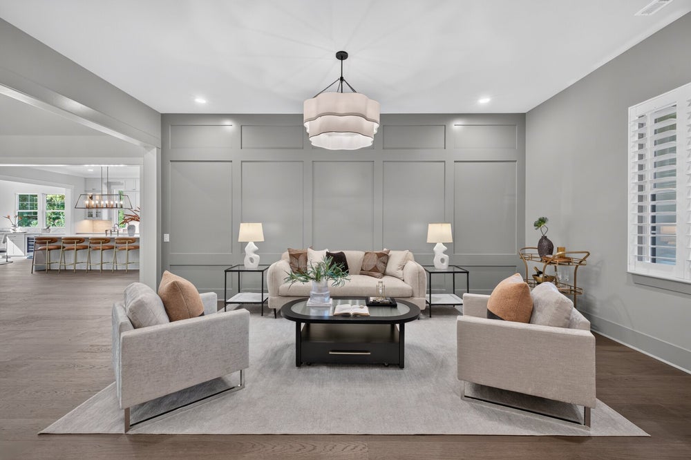 Living room with gray panel walls, neutral seating, dark coffee table, and pendant light over hardwood floors