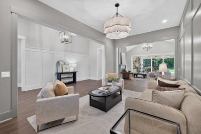 Formal living room with neutral sofas, dark oval coffee table, wainscoting, and large pendant light over hardwood floors