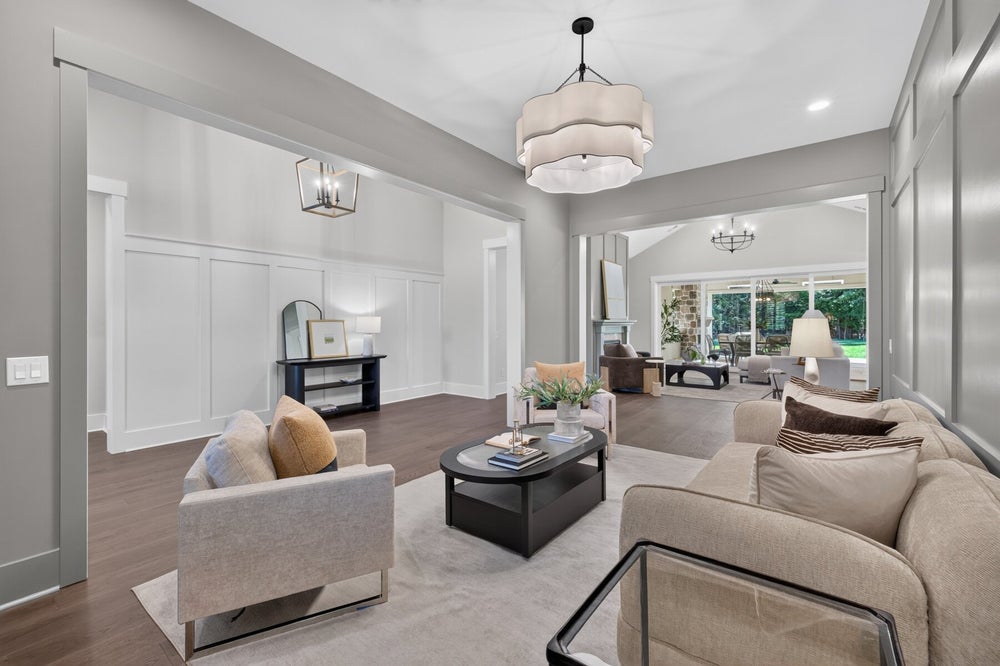 Formal living room with neutral sofas, dark oval coffee table, wainscoting, and large pendant light over hardwood floors