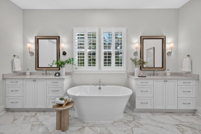 Master bathroom with freestanding soaking tub, dual white vanities, and marble tile floors