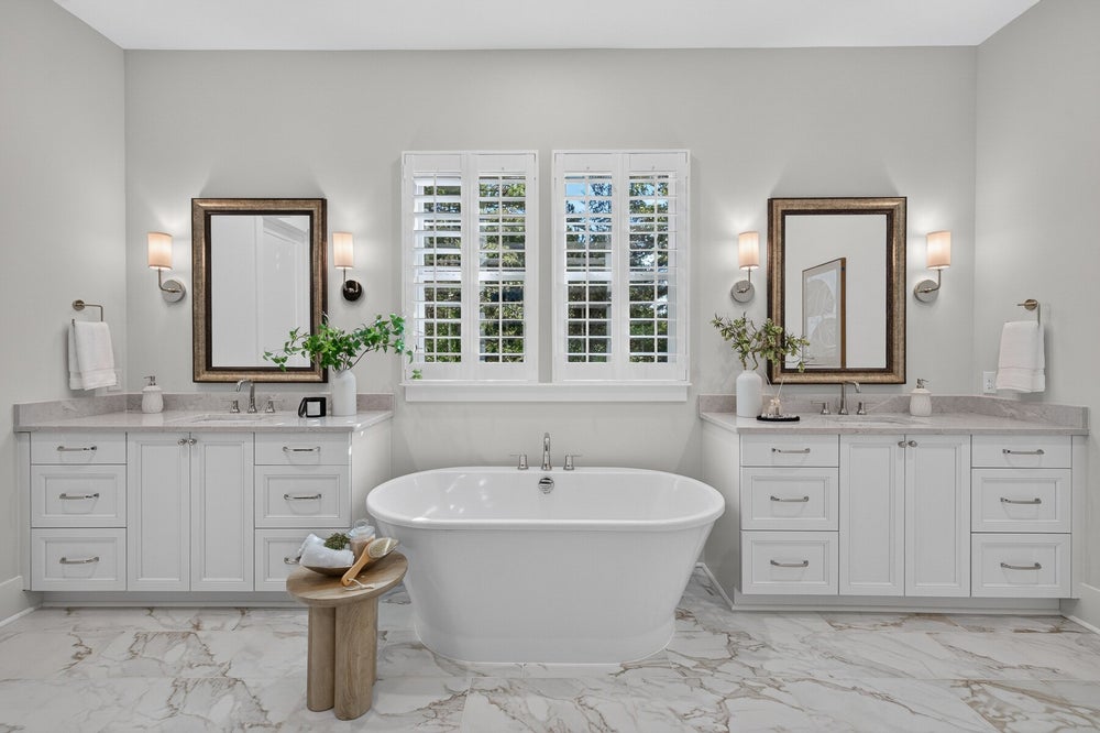 Master bathroom with freestanding soaking tub, dual white vanities, and marble tile floors