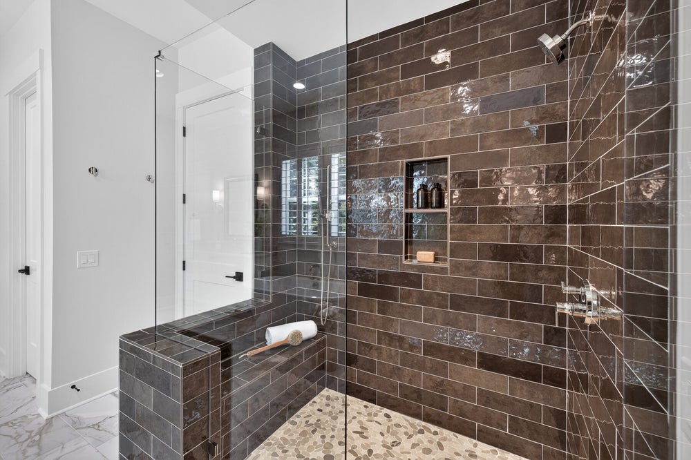 Walk-in shower with dark brown subway tiles, glass enclosure, built-in niche, and tiled bench seat