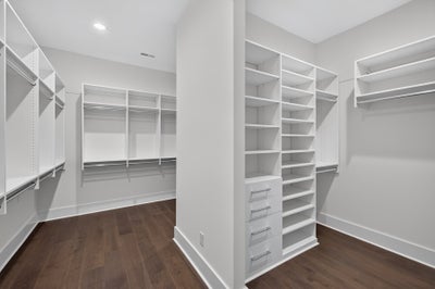 Large walk-in closet with white built-in shelving, hanging rods, drawers, and dark hardwood floors