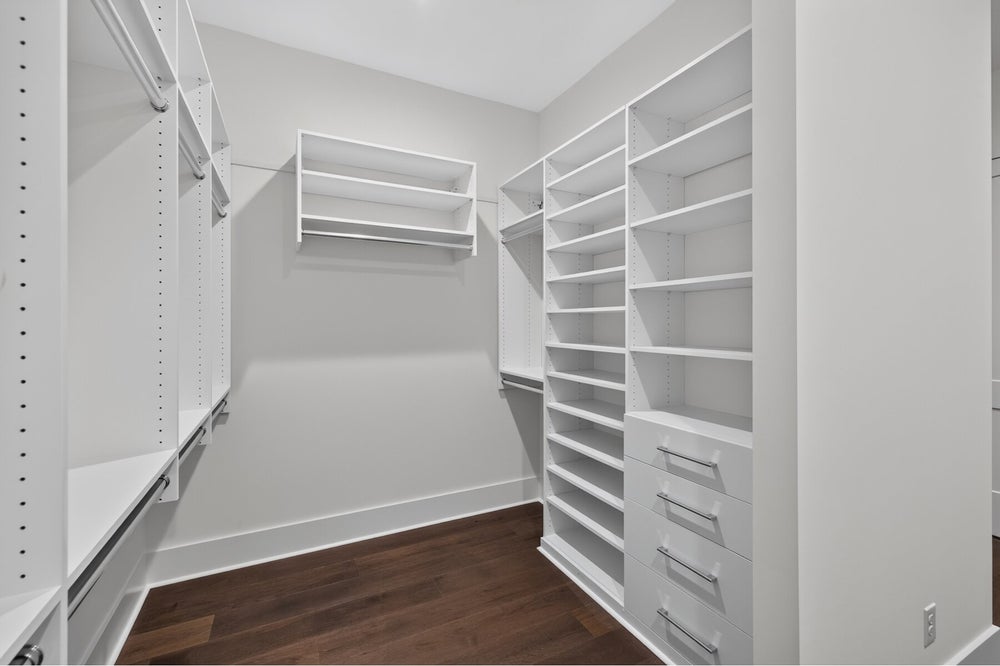 Walk-in closet with white built-in shelving, hanging rods, drawers, and dark hardwood floors