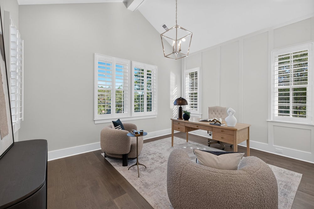 Home office with vaulted ceiling, wood desk, plantation shutters, and hardwood floors