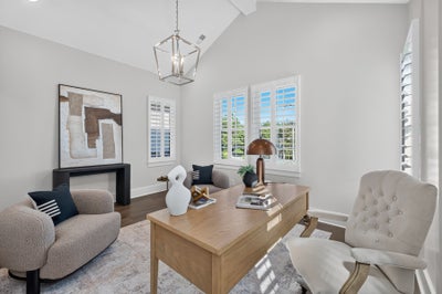 Home office with vaulted ceiling, wood desk, tufted chair, and plantation shutters on multiple windows