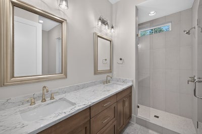 Bathroom with double sink vanity, marble countertop, wood cabinets, and walk-in tile shower with glass enclosure